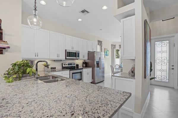 kitchen with a sink, white cabinets, light stone counters, and stainless steel appliances