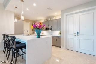 kitchen with stainless steel microwave, a kitchen breakfast bar, hanging light fixtures, light countertops, and a sink