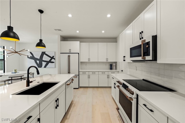 kitchen with white appliances, white cabinets, a sink, and decorative light fixtures