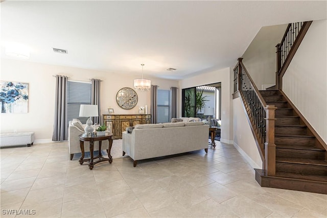 living room featuring visible vents, stairway, a chandelier, and baseboards