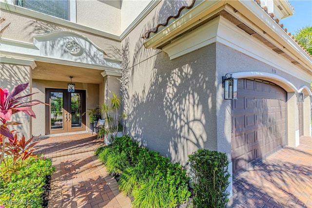 view of exterior entry featuring french doors, an attached garage, and stucco siding