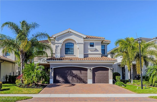 mediterranean / spanish home with decorative driveway, an attached garage, a tile roof, and stucco siding