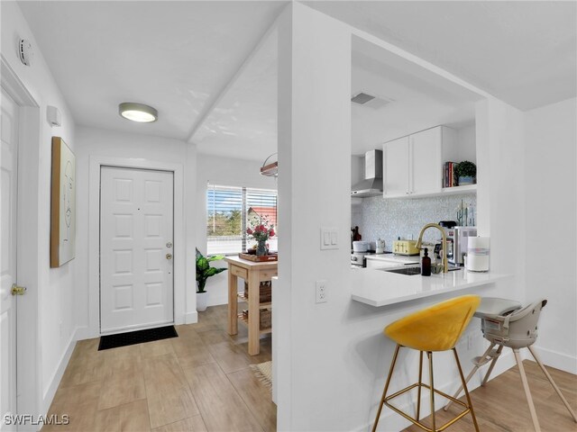 9831 Alabama St Unit 5, Bonita Springs, FL 34135 - kitchen featuring wall chimney exhaust hood, a breakfast bar, sink, white cabinetry, and decorative backsplash