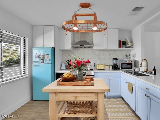 kitchen with sink, fridge, backsplash, wall chimney range hood, and white cabinets