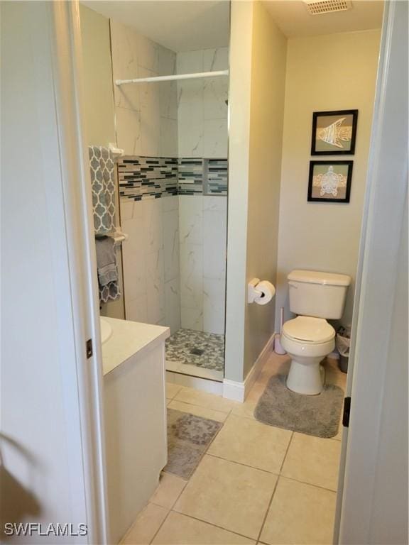 bathroom with tile patterned flooring, vanity, toilet, and tiled shower