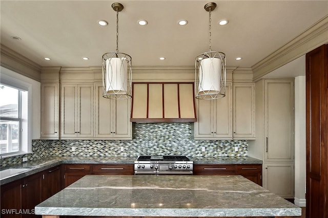 kitchen with light stone counters, cream cabinets, stainless steel range oven, a kitchen island, and decorative light fixtures