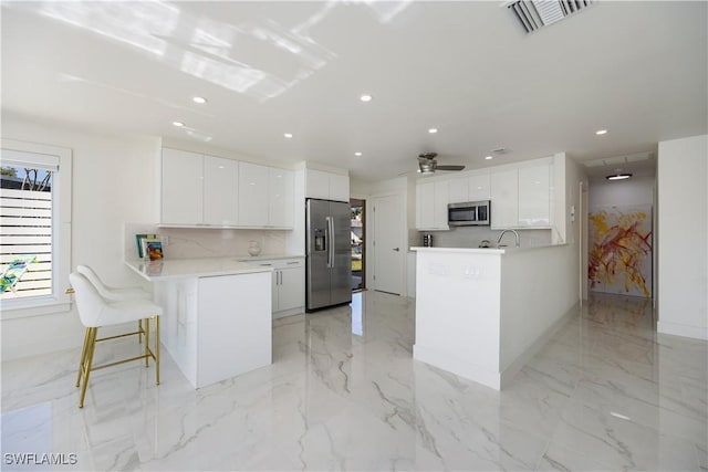 kitchen with stainless steel appliances, white cabinetry, a breakfast bar area, and backsplash