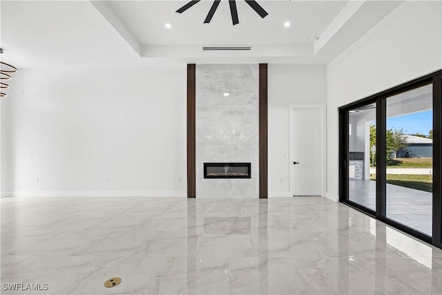 unfurnished living room with ceiling fan, a fireplace, and a tray ceiling