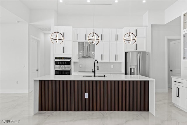 kitchen featuring wall chimney exhaust hood, sink, appliances with stainless steel finishes, a kitchen island with sink, and white cabinets