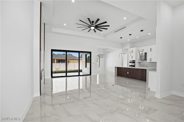 unfurnished living room with a towering ceiling, a raised ceiling, and ceiling fan