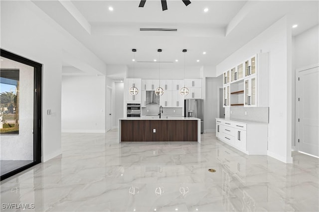 kitchen with an island with sink, pendant lighting, stainless steel appliances, decorative backsplash, and white cabinets