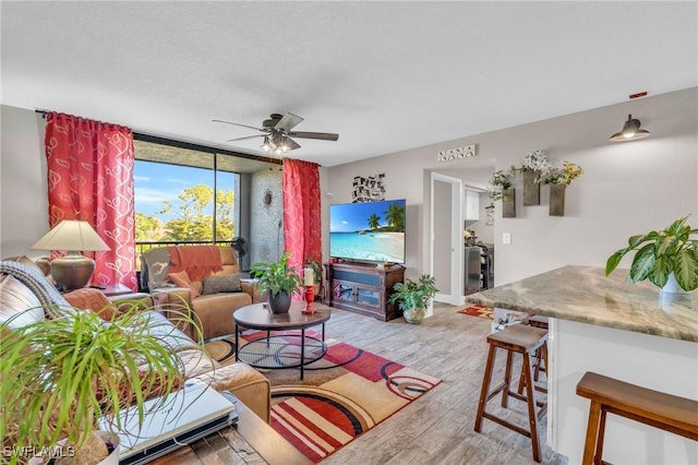 living room with ceiling fan, a wall of windows, light hardwood / wood-style floors, and a textured ceiling