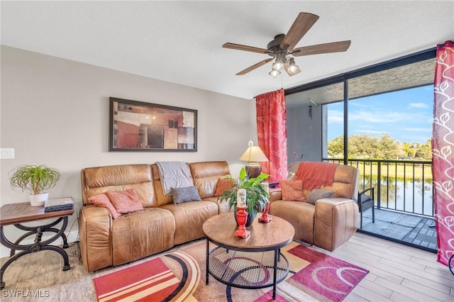 living room with light wood-type flooring, floor to ceiling windows, ceiling fan, and a water view