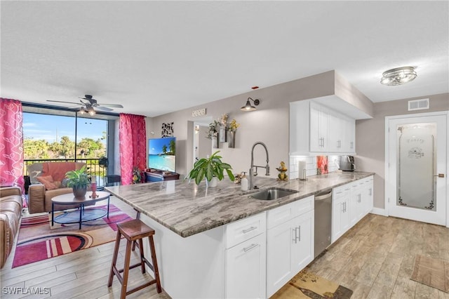 kitchen with sink, white cabinetry, light stone countertops, stainless steel dishwasher, and kitchen peninsula