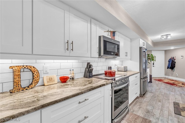 kitchen featuring tasteful backsplash, appliances with stainless steel finishes, light stone countertops, light hardwood / wood-style floors, and white cabinets