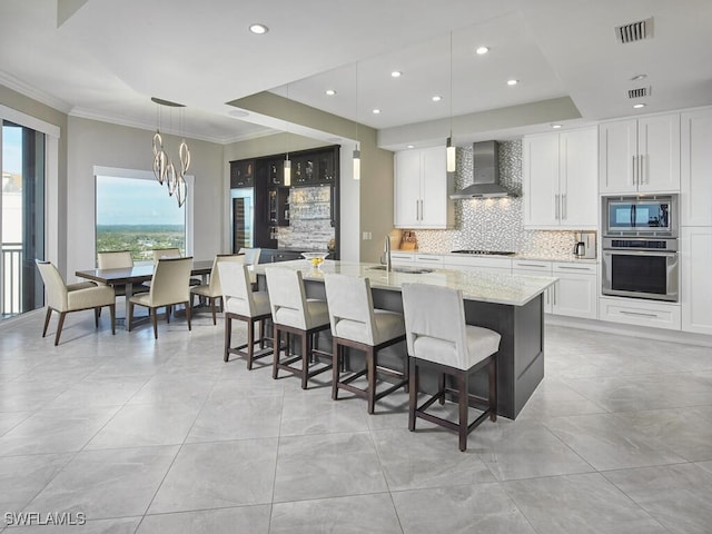 kitchen featuring appliances with stainless steel finishes, white cabinetry, hanging light fixtures, light stone countertops, and wall chimney exhaust hood