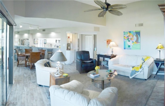 living room with rail lighting, a towering ceiling, ceiling fan, and light hardwood / wood-style floors