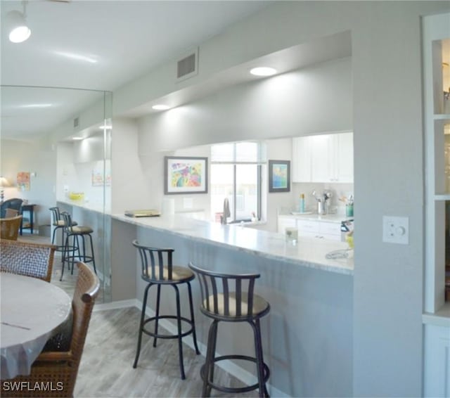 kitchen featuring white cabinetry, light hardwood / wood-style flooring, a kitchen breakfast bar, and kitchen peninsula