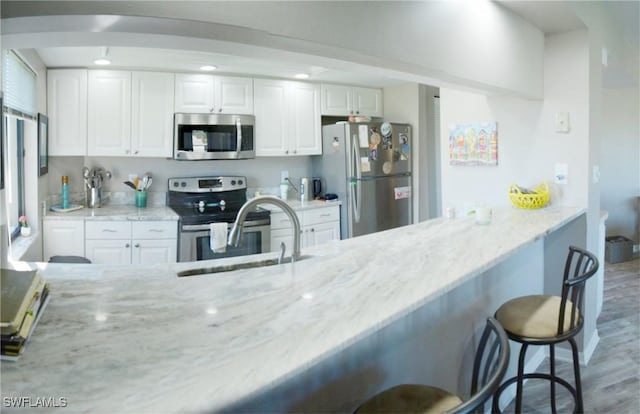 kitchen with sink, white cabinetry, wood-type flooring, a kitchen breakfast bar, and stainless steel appliances