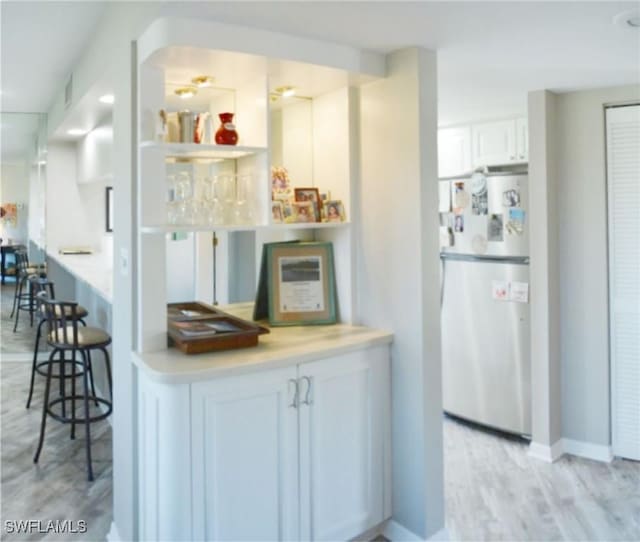 kitchen featuring stainless steel fridge, a breakfast bar, light hardwood / wood-style flooring, and white cabinets