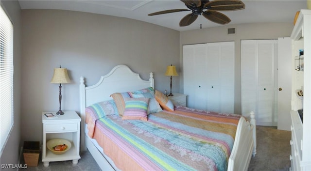 bedroom featuring ceiling fan, dark carpet, and two closets