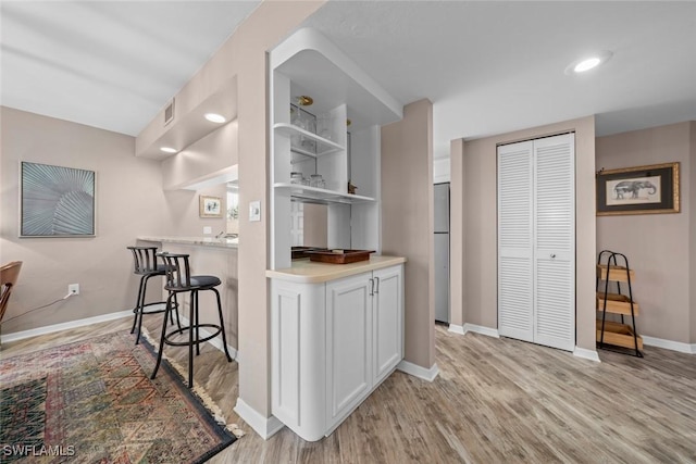 kitchen with stainless steel fridge, white cabinets, a kitchen bar, and light hardwood / wood-style flooring