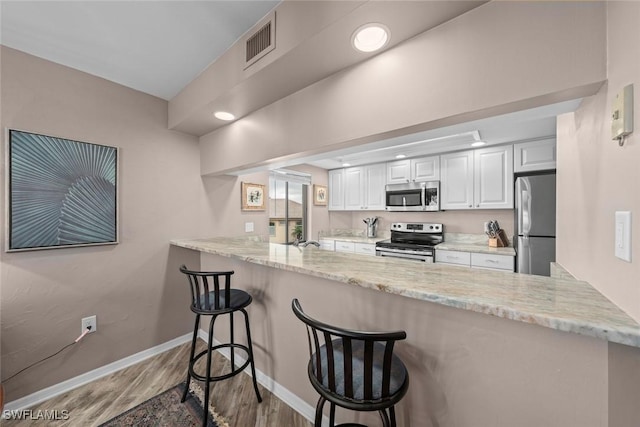 kitchen with a breakfast bar area, white cabinetry, appliances with stainless steel finishes, kitchen peninsula, and light hardwood / wood-style floors