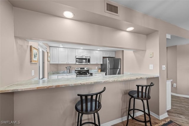 kitchen featuring white cabinetry, appliances with stainless steel finishes, a breakfast bar area, and kitchen peninsula