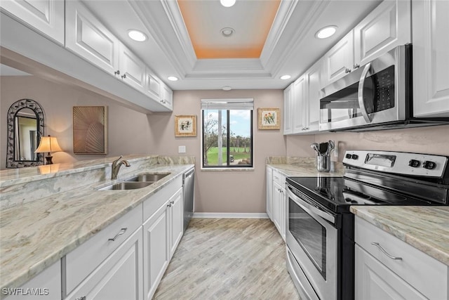 kitchen with appliances with stainless steel finishes, sink, white cabinets, ornamental molding, and a raised ceiling