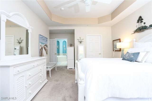 carpeted bedroom featuring a tray ceiling, ceiling fan, and ensuite bathroom