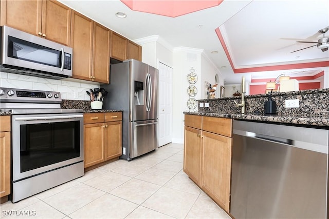 kitchen with appliances with stainless steel finishes, tasteful backsplash, dark stone counters, ornamental molding, and light tile patterned floors