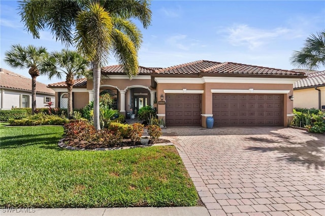 mediterranean / spanish-style house with decorative driveway, a tile roof, stucco siding, a front yard, and a garage