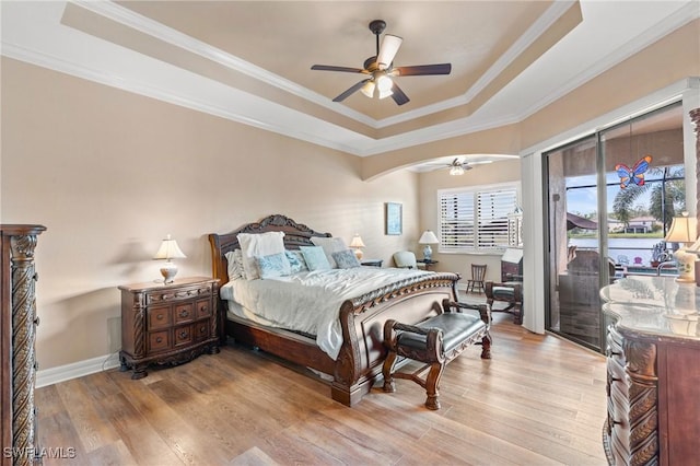 bedroom with access to outside, a tray ceiling, light wood-type flooring, and crown molding