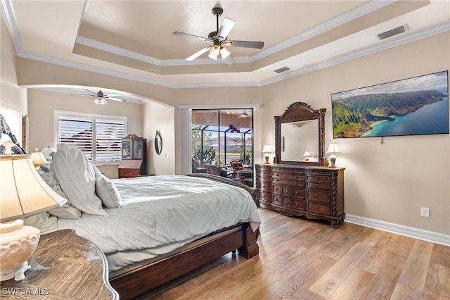 bedroom with access to exterior, a tray ceiling, multiple windows, and wood finished floors