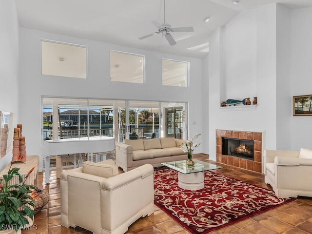 living room with a tile fireplace, ceiling fan, and high vaulted ceiling