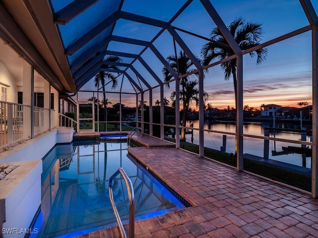 pool at dusk featuring a patio, a water view, a dock, and glass enclosure