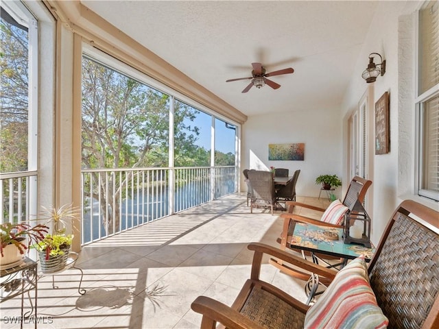 sunroom featuring ceiling fan and a water view