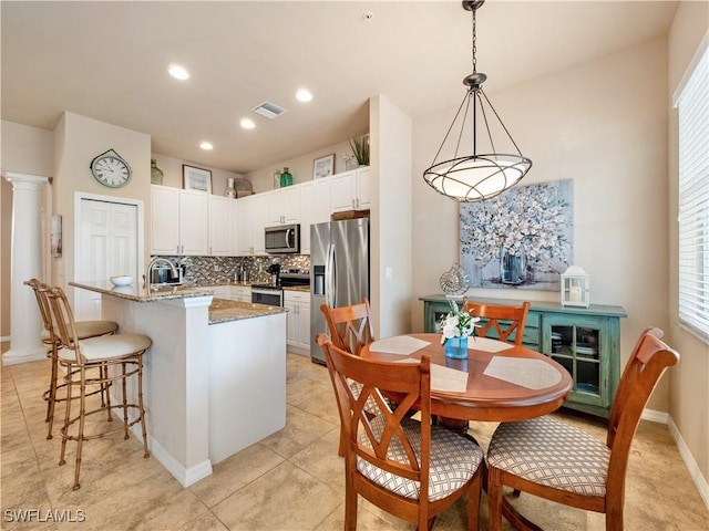 kitchen with appliances with stainless steel finishes, white cabinetry, a kitchen island with sink, light stone counters, and decorative light fixtures