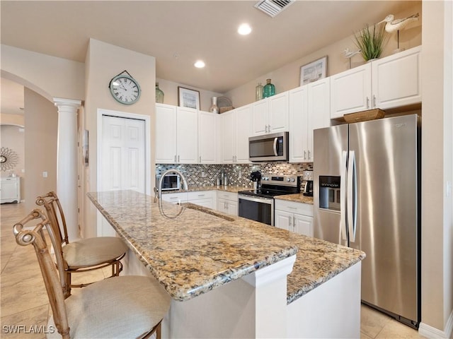 kitchen with stainless steel appliances, light stone countertops, and a center island with sink