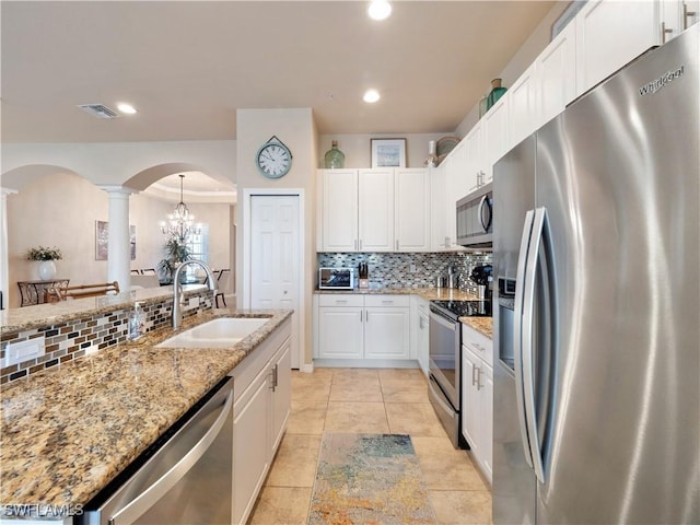 kitchen featuring sink, white cabinetry, stainless steel appliances, light stone countertops, and decorative light fixtures