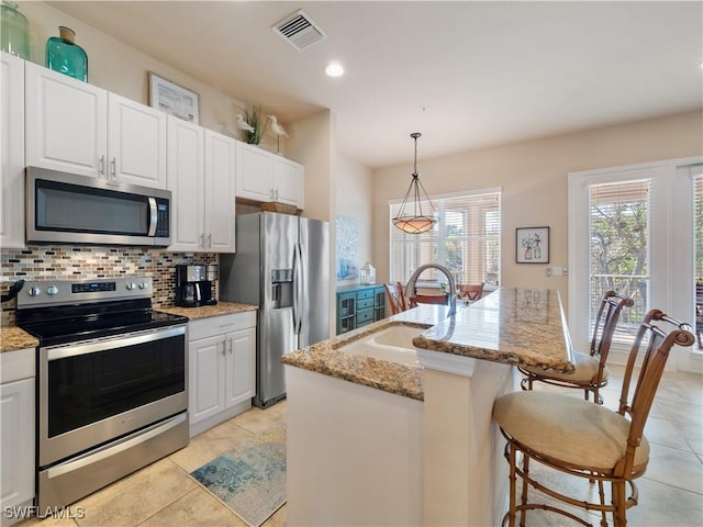 kitchen featuring pendant lighting, sink, appliances with stainless steel finishes, white cabinetry, and an island with sink