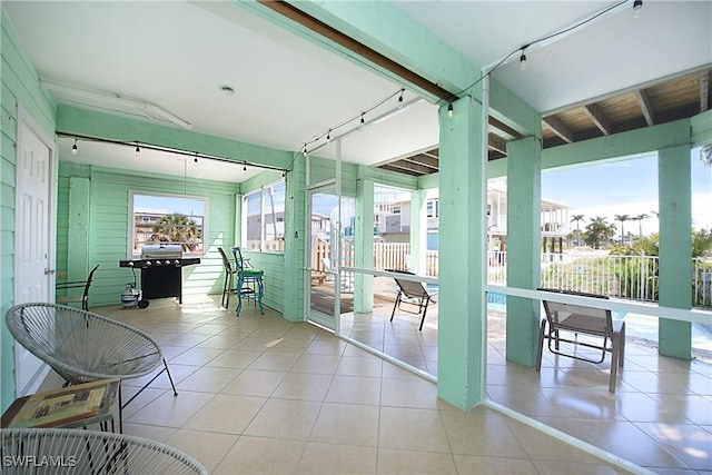 sunroom / solarium featuring beamed ceiling and track lighting