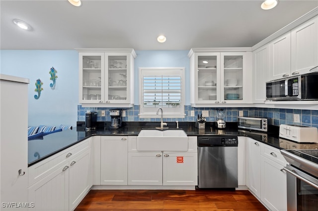 kitchen featuring appliances with stainless steel finishes, sink, white cabinets, backsplash, and dark wood-type flooring