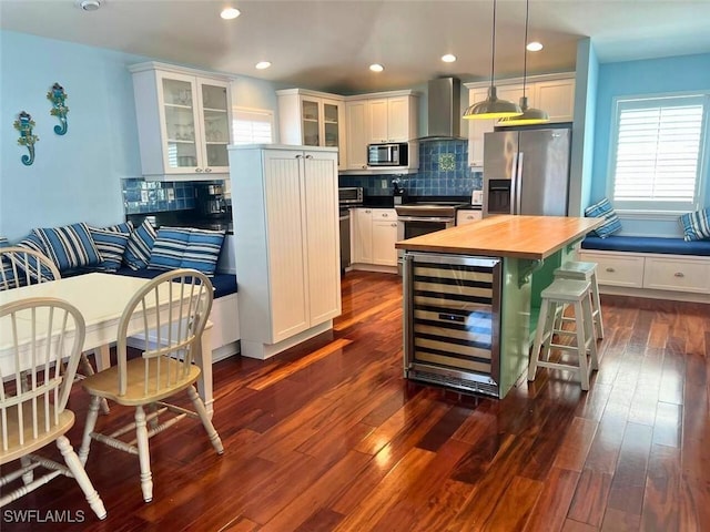 kitchen with wine cooler, white cabinetry, appliances with stainless steel finishes, a kitchen island, and wall chimney range hood