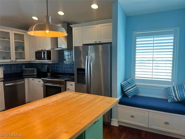 kitchen with pendant lighting, wood counters, white cabinets, stainless steel appliances, and wall chimney range hood