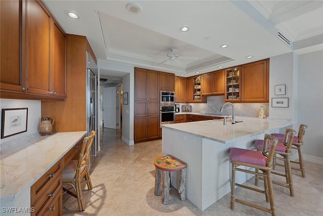 kitchen with a breakfast bar area, brown cabinetry, a peninsula, and a raised ceiling