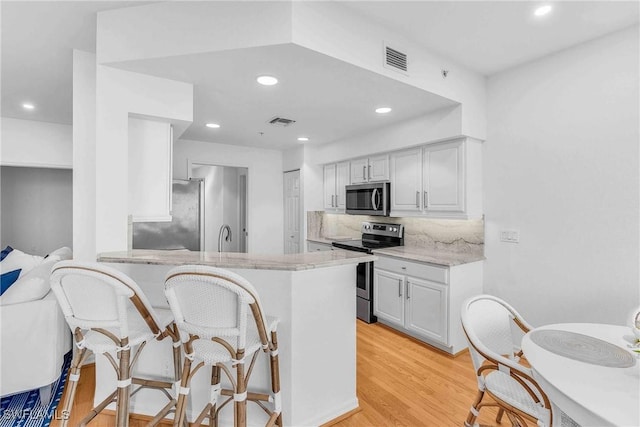 kitchen with stainless steel appliances, decorative backsplash, light hardwood / wood-style floors, and kitchen peninsula