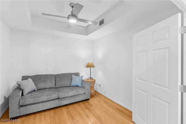 living room featuring wood-type flooring, ceiling fan, and a tray ceiling