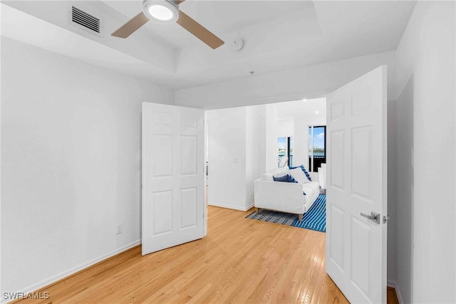 bedroom with light hardwood / wood-style flooring, a raised ceiling, and ceiling fan