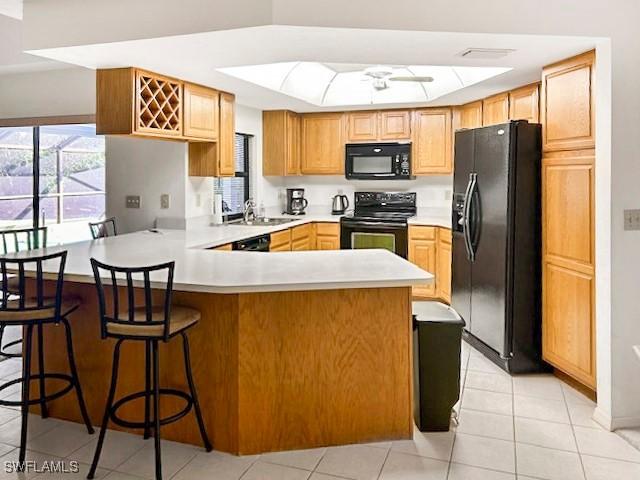 kitchen featuring sink, light tile patterned floors, a kitchen breakfast bar, kitchen peninsula, and black appliances